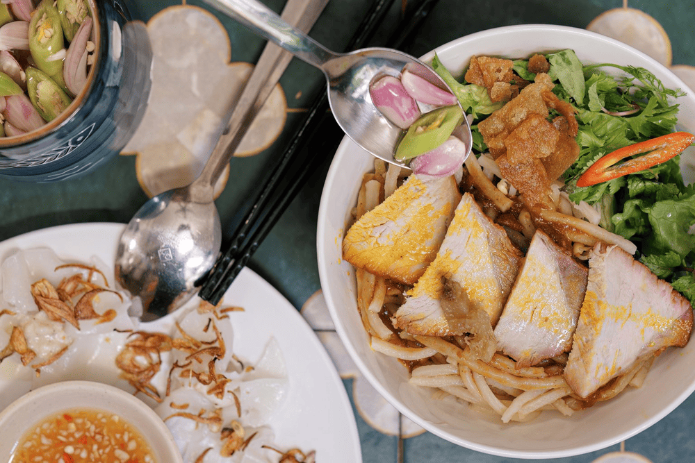A flavorful bowl of Hoi An's iconic cao lau, where smoky pork meets crispy toppings and fresh herbs (Source: Qu&aacute;n Cao lầu B&aacute; Lễ - Qu&aacute;n Cao lầu ngon tại Hội An)